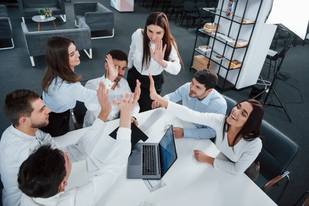 giving high five each other top view office workers classic wear sitting near table using laptop documents